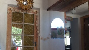 A wooden door with a sunburst mirror above it, a string of white lights, and a small window with a view of the outside. - 110m2 house + pool, No neighbors, in the countryside between Uzès and Cévennes (Occitanie)
