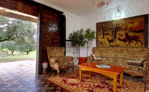 Traditional room with a sofa, armchair, and coffee table, featuring a large tapestry and a potted plant.