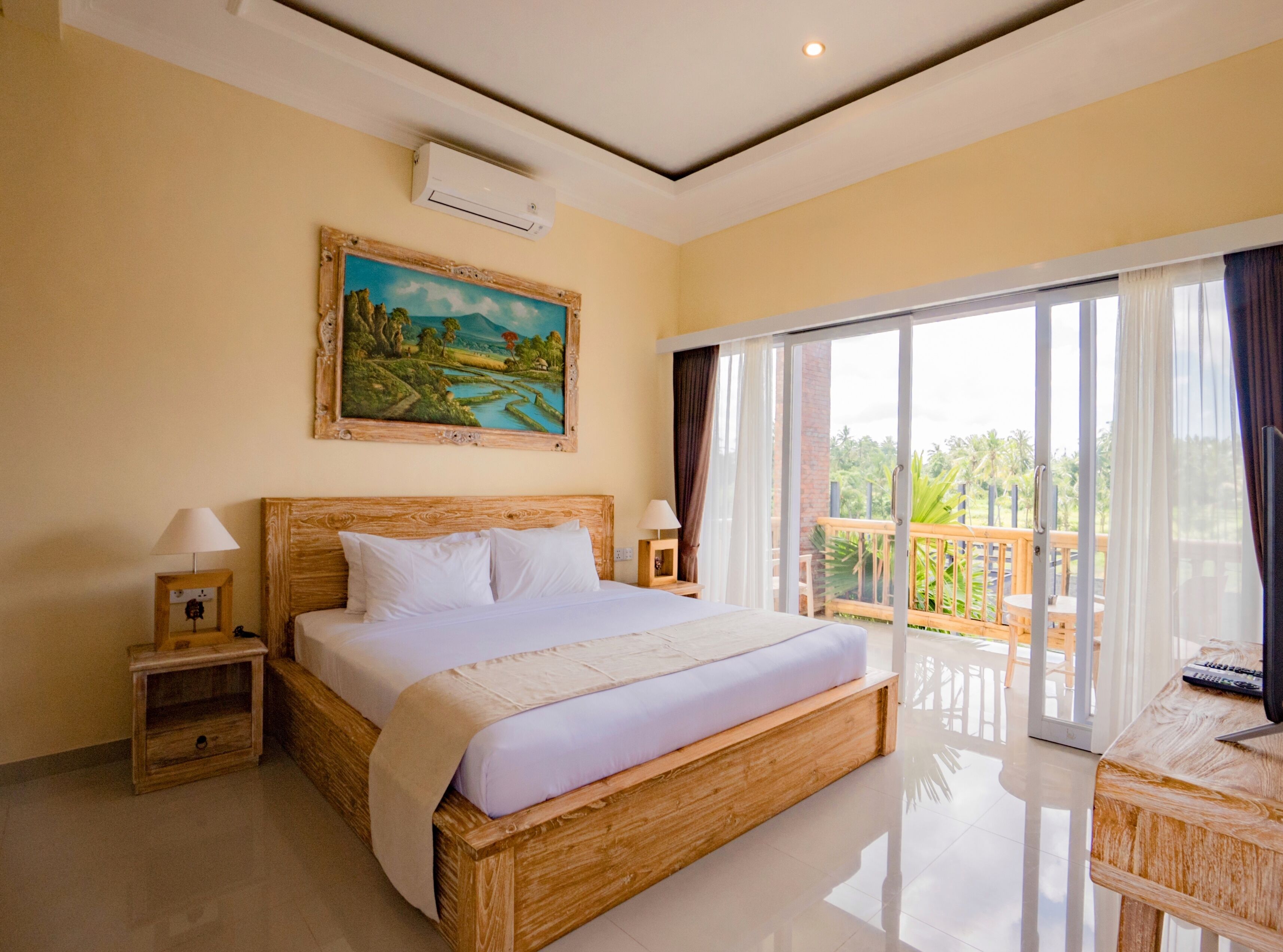 Quarto com uma cama grande, um quadro, ar-condicionado, mesa de cabeceira, abajur e varanda com vista.