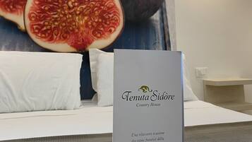 A hotel room with a large poster of figs, a white bed, and a sign reading "Tenuta Sidore Country House".