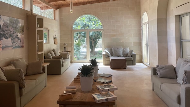 A spacious living room with a high wooden ceiling, a large arched doorway leading outside, and a cozy seating area with sofas and a coffee table. - Tenuta Sidore (Cursi)