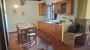 A kitchen with wooden cabinets, a dining table set for six, and a stone fireplace. - House with private garden in the Crete Senesi (Asciano)