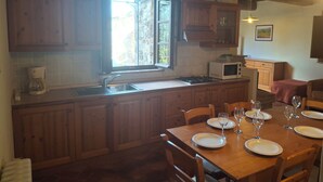 A kitchen with wooden cabinets, a window, a microwave, and a dining table set for four with wine glasses. - House with private garden in the Crete Senesi (Asciano)