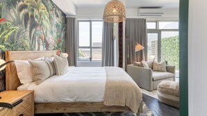 Ein Schlafzimmer mit einem großen Bett, einem Sofa, einer Hängeleuchte und Blick auf die Stadt durch große Fenster.