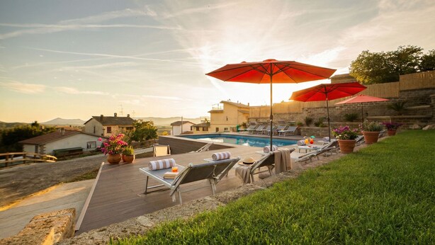 A poolside area with lounge chairs, umbrellas, and potted plants.
