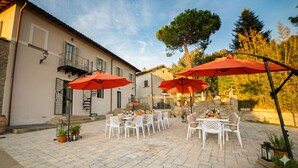 An outdoor patio with white tables and red umbrellas, surrounded by stone walls and potted plants.