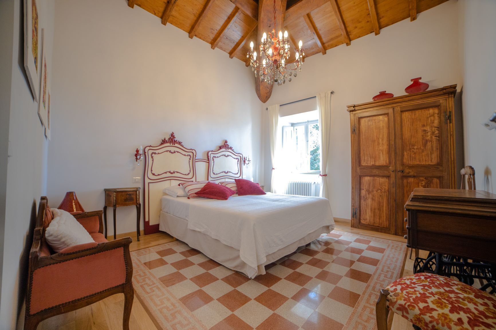 Un dormitorio con suelo a cuadros, una cama con ropa de cama blanca y rosa, un armario de madera y una araña.