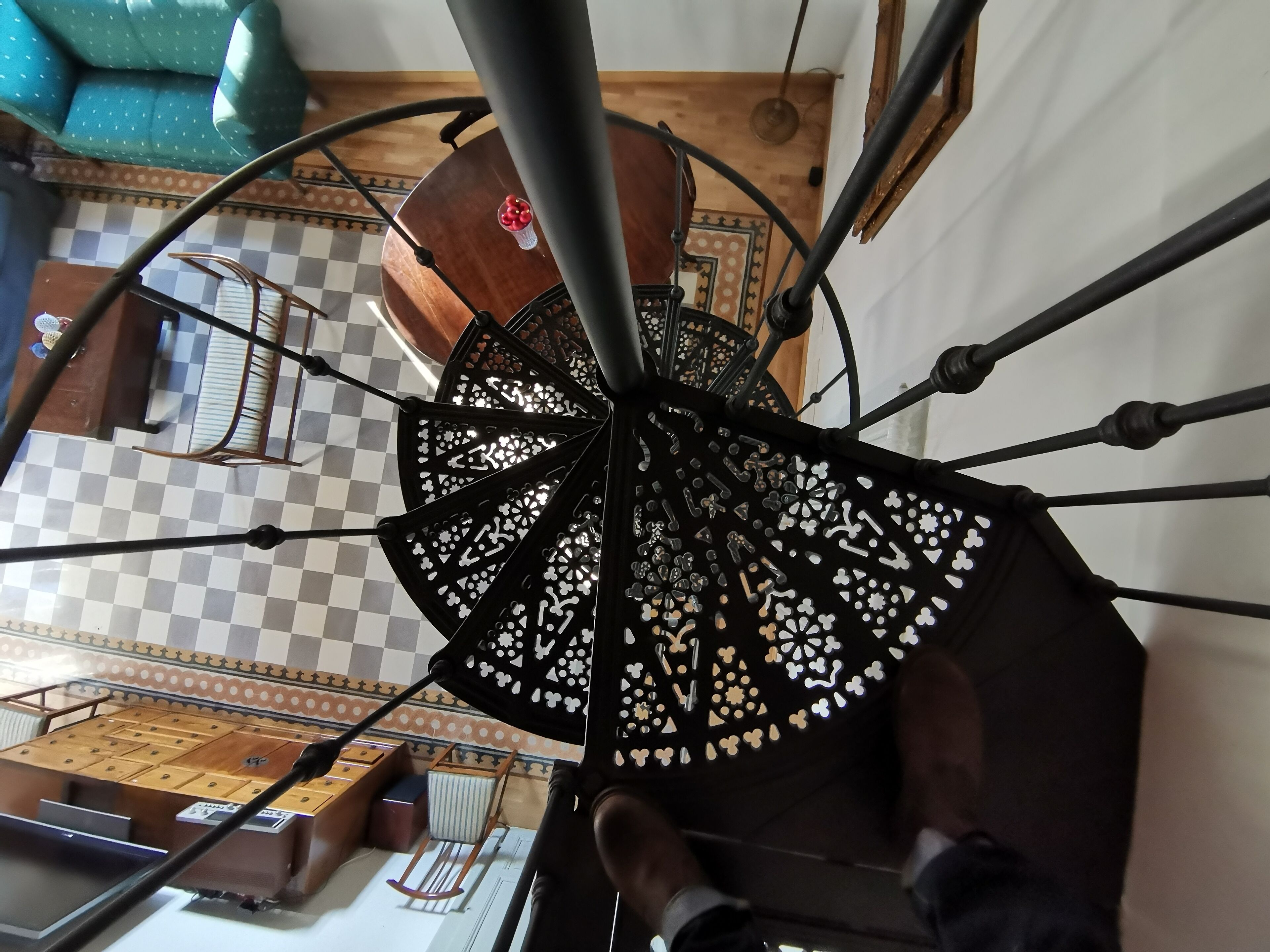 A spiral staircase with a decorative metal railing and patterned floor tiles.