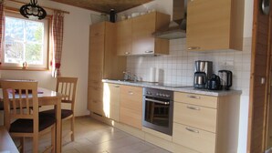 Una cocina con armarios de madera, estufa, pileta y una ventana con cortinas.