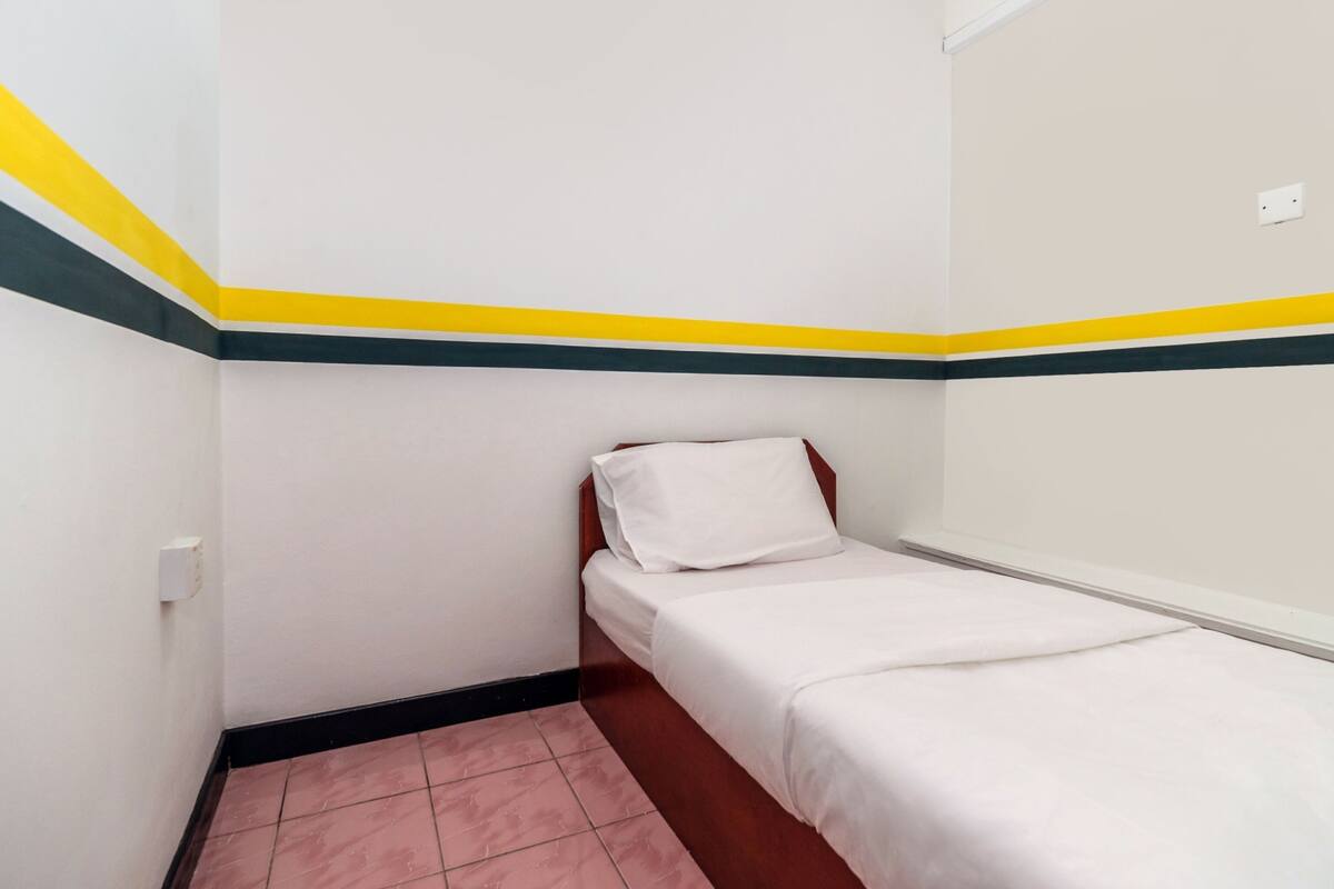 A small, single-bed room with white walls, a yellow and green stripe, and a pink-tiled floor.