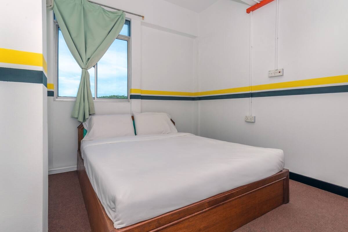 A single bed in a room with a window, a power outlet on the wall, and a striped wall design.