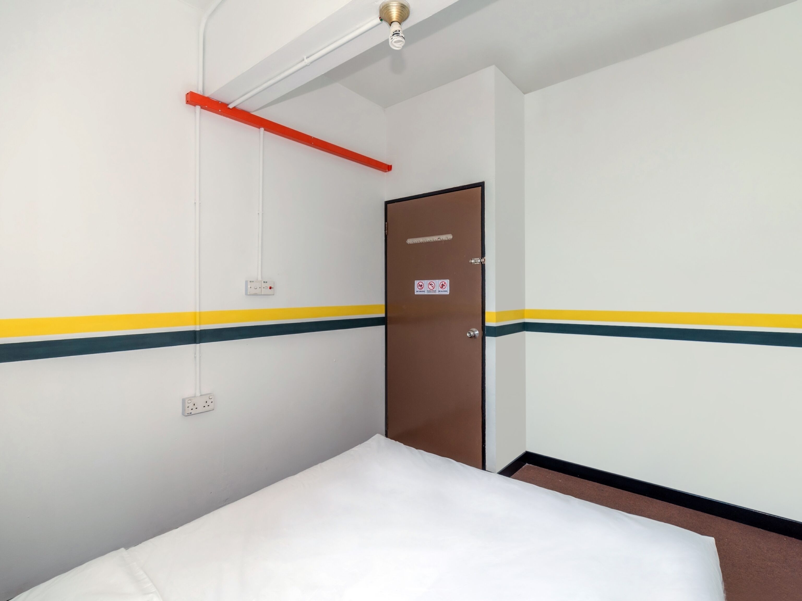 A hotel room with a bed, a door, and a light fixture.