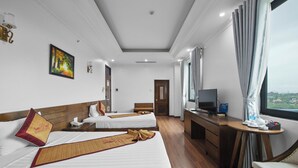 A hotel room with two beds, a desk with a television, and a window with curtains.