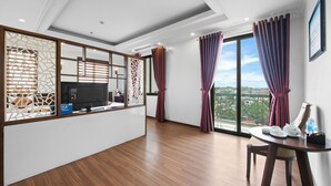 A modern hotel room with a wooden floor, a flat-screen TV, a small table with a teapot and cups, and a large window with curtains.