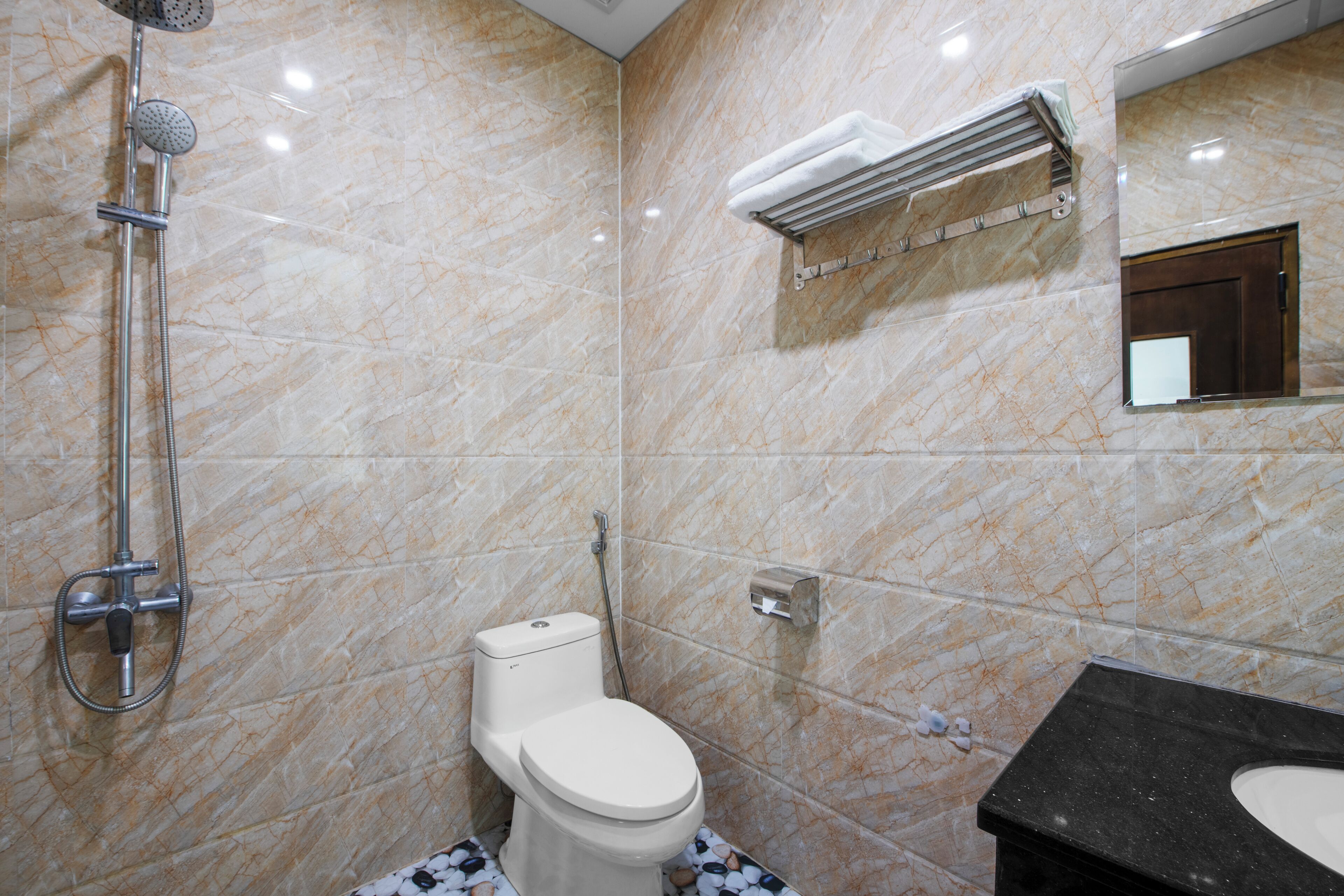 A bathroom with a marble wall, a toilet, a shower, and a sink.