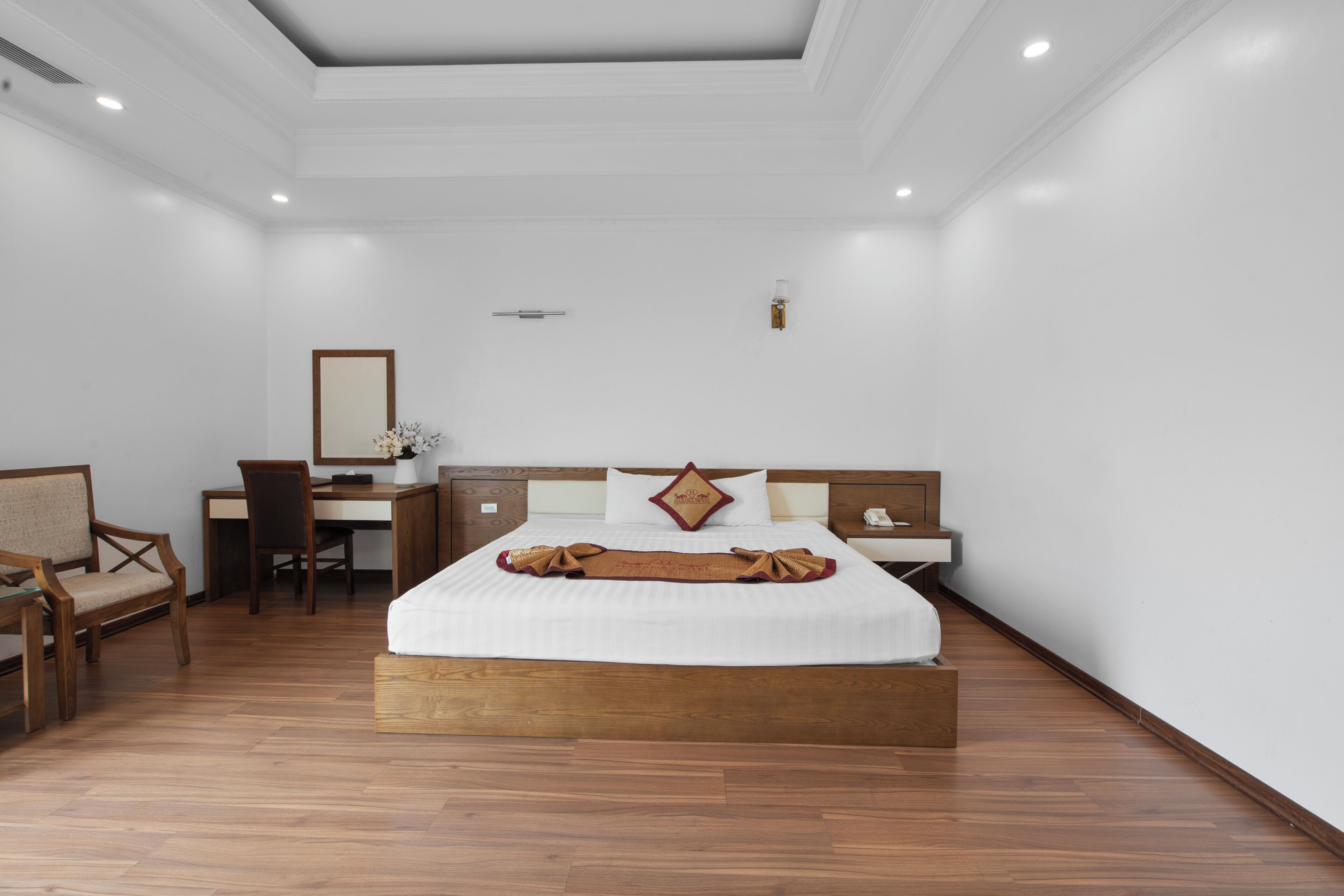 A hotel room with a wooden bed, a desk, a chair, and a mirror.