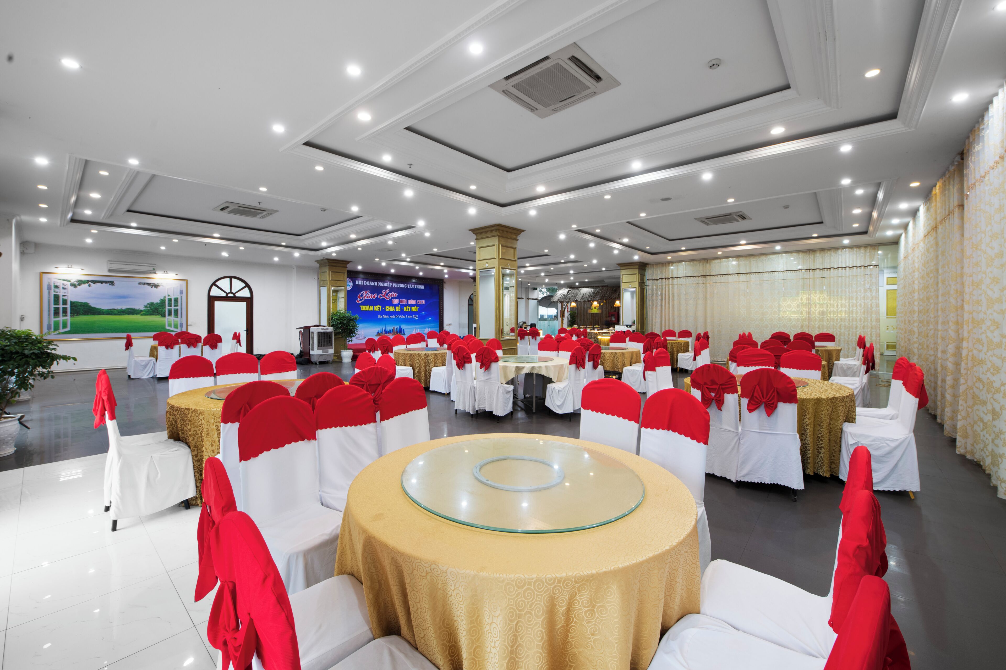 A banquet hall with round tables covered in gold tablecloths and white chairs with red sashes.