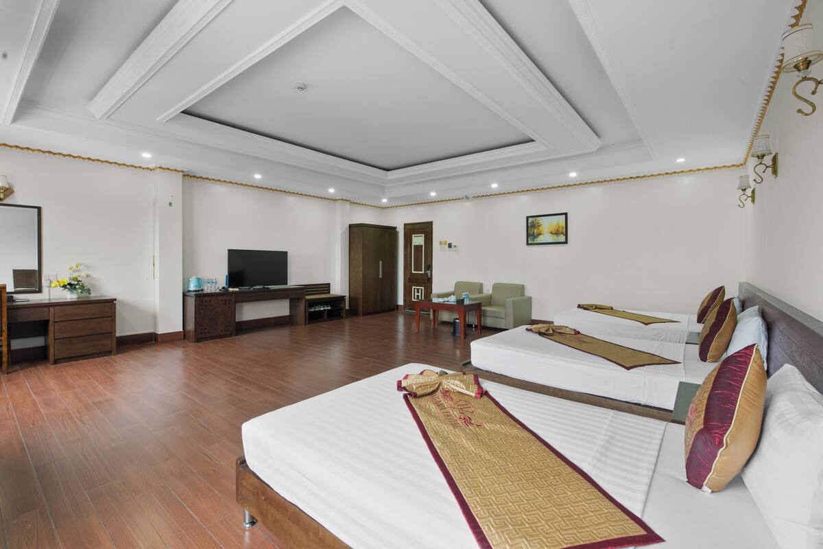 A hotel room with two beds, a desk, a TV, and a seating area.