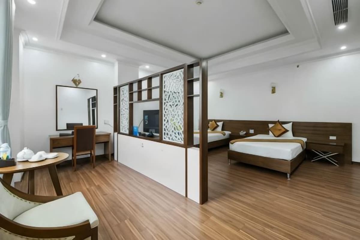 Habitació d'hotel amb sòl de fusta, escriptori amb cadira, llit amb capçal i separador amb pantalla decorativa.