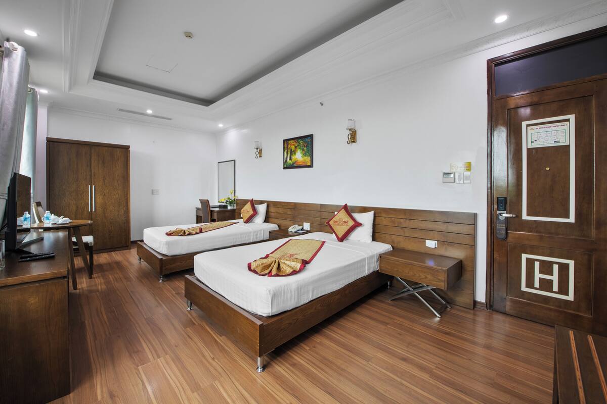A hotel room with two beds, a desk, a chair, a wardrobe, and a bathroom.