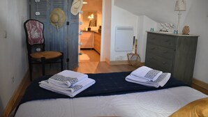 Un dormitorio con cama, una silla, un aparador y una puerta que da a otra habitación.