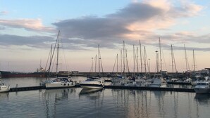 A marina with multiple boats docked, calm water, and a clear sky.