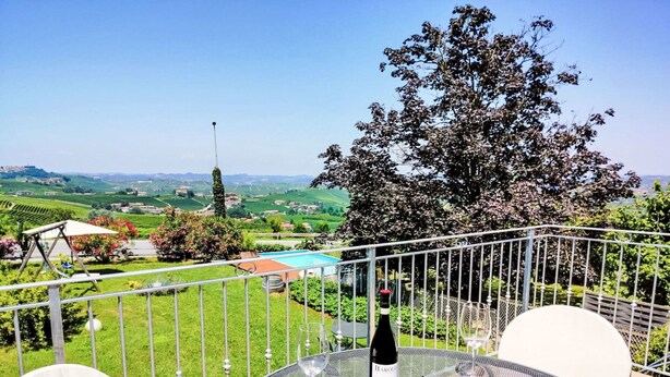 A balcony with a table, a bottle of wine, and a glass. - Lovely apartment for 2 people with pool, WIFI, TV, patio and pets allowed (La Morra)