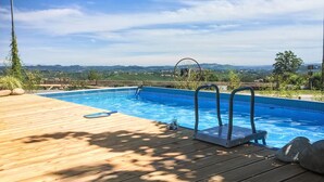 A wooden deck with a swimming pool, surrounded by greenery and a scenic view of distant hills. - Lovely apartment for 2 people with pool, WIFI, TV, patio and pets allowed (La Morra)