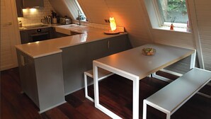 Una cocina moderna con una isla central, una mesa de comedor con bancos y una ventana con vistas a la vegetación.