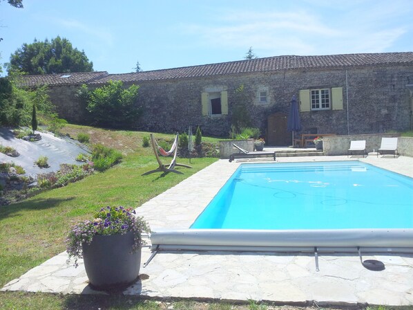 A swimming pool with a stone deck, a hammock, and a potted plant.