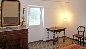 Quarto com cômoda, espelho, mesa de cabeceira com abajur, cadeira e cama com manta listrada.