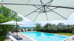 A swimming pool with lounge chairs and umbrellas, surrounded by a wooden deck and greenery. - Nice apartment in villa for 6 people with pool, WIFI, TV and terrace (Atessa)