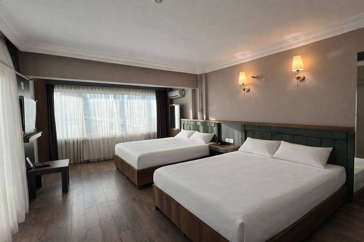 Ein Hotelzimmer mit zwei Betten, einem Fernseher, einem Schreibtisch und einem Fenster mit Vorhängen.