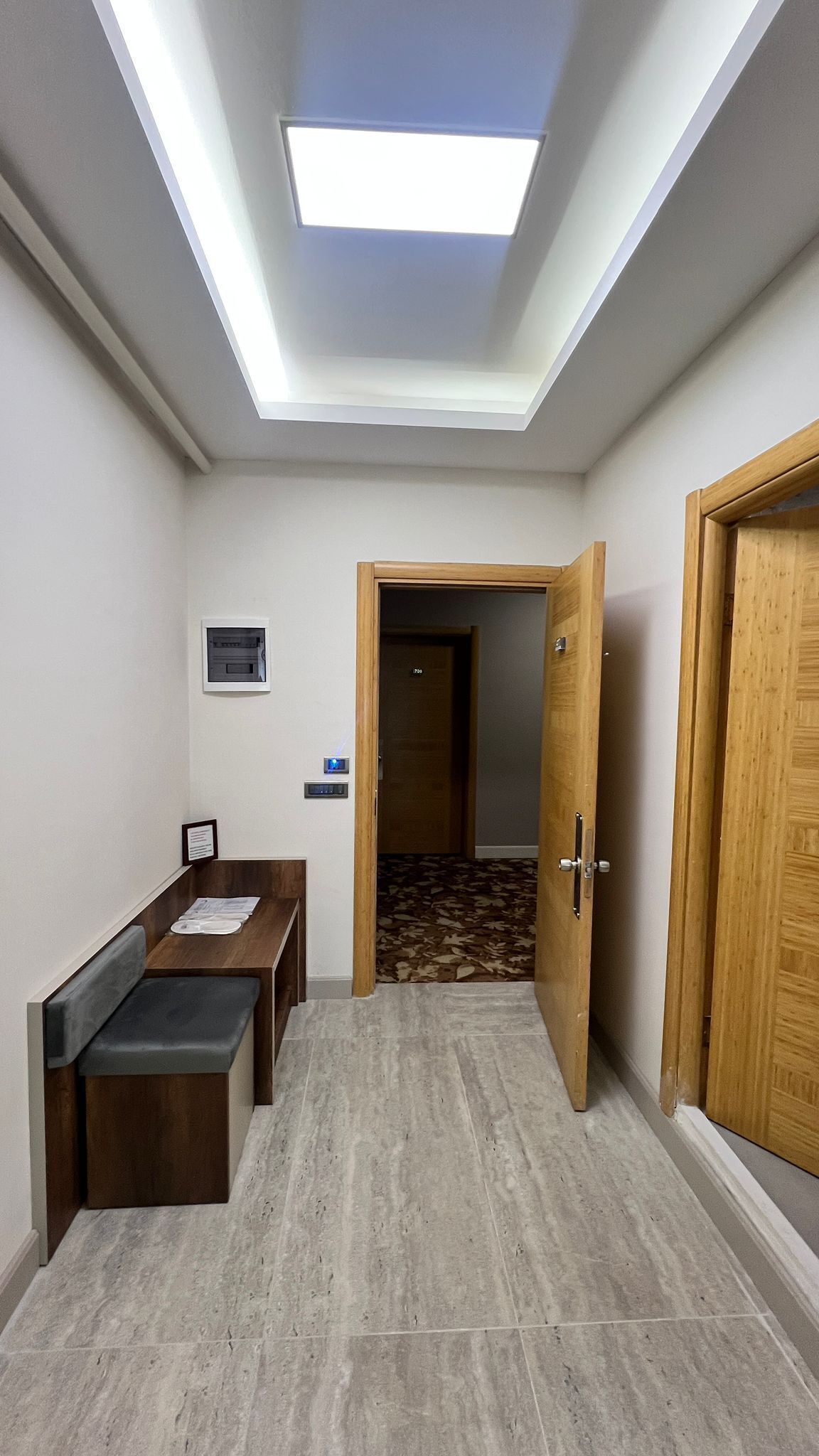 A hallway with a skylight, a bench, a small table, and a door leading to another room.