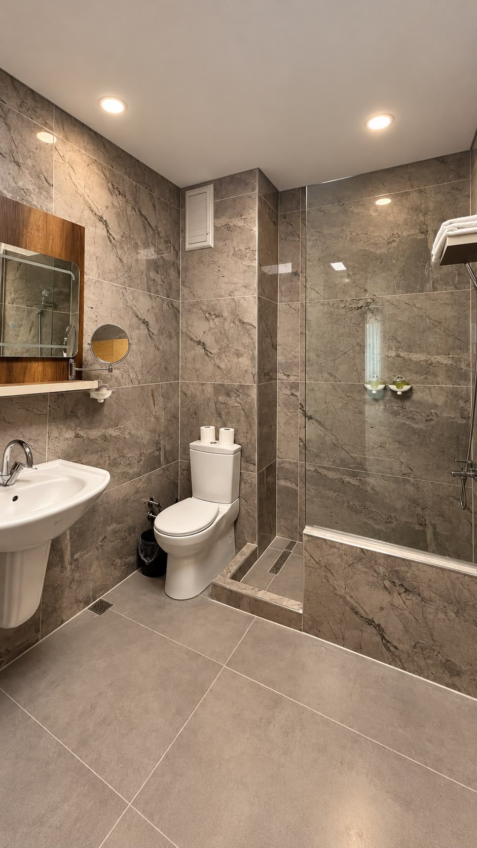 A modern bathroom with a marble wall, a sink, a toilet, and a shower area.