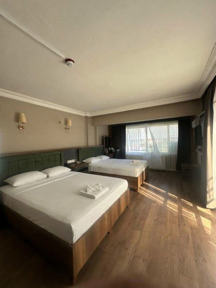 A hotel room with two beds, a flat-screen TV, a bedside table, and a window with curtains.
