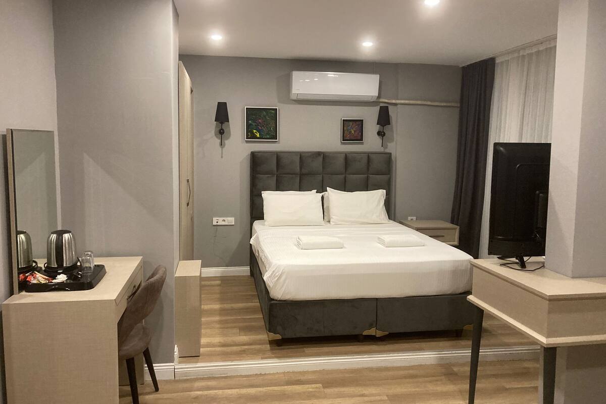 Ein modernes Hotelzimmer mit Bett, Nachttisch, Schreibtisch, Stuhl und Fernseher.