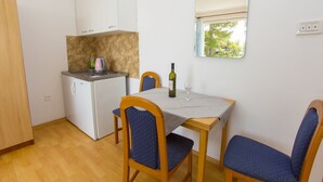 Uma cozinha compacta com uma mesa de jantar, cadeiras, geladeira e uma janela com vista para árvores.