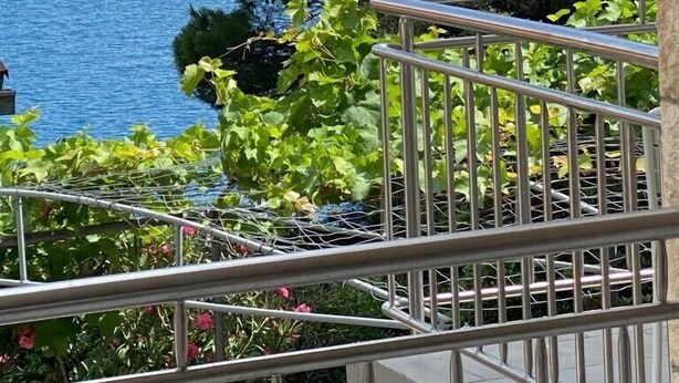 Varanda com grade de metal, vista para a água e vegetação.
