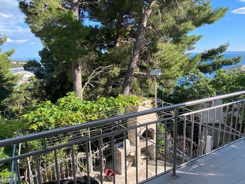 A metal railing overlooking a garden with trees and a stone structure.