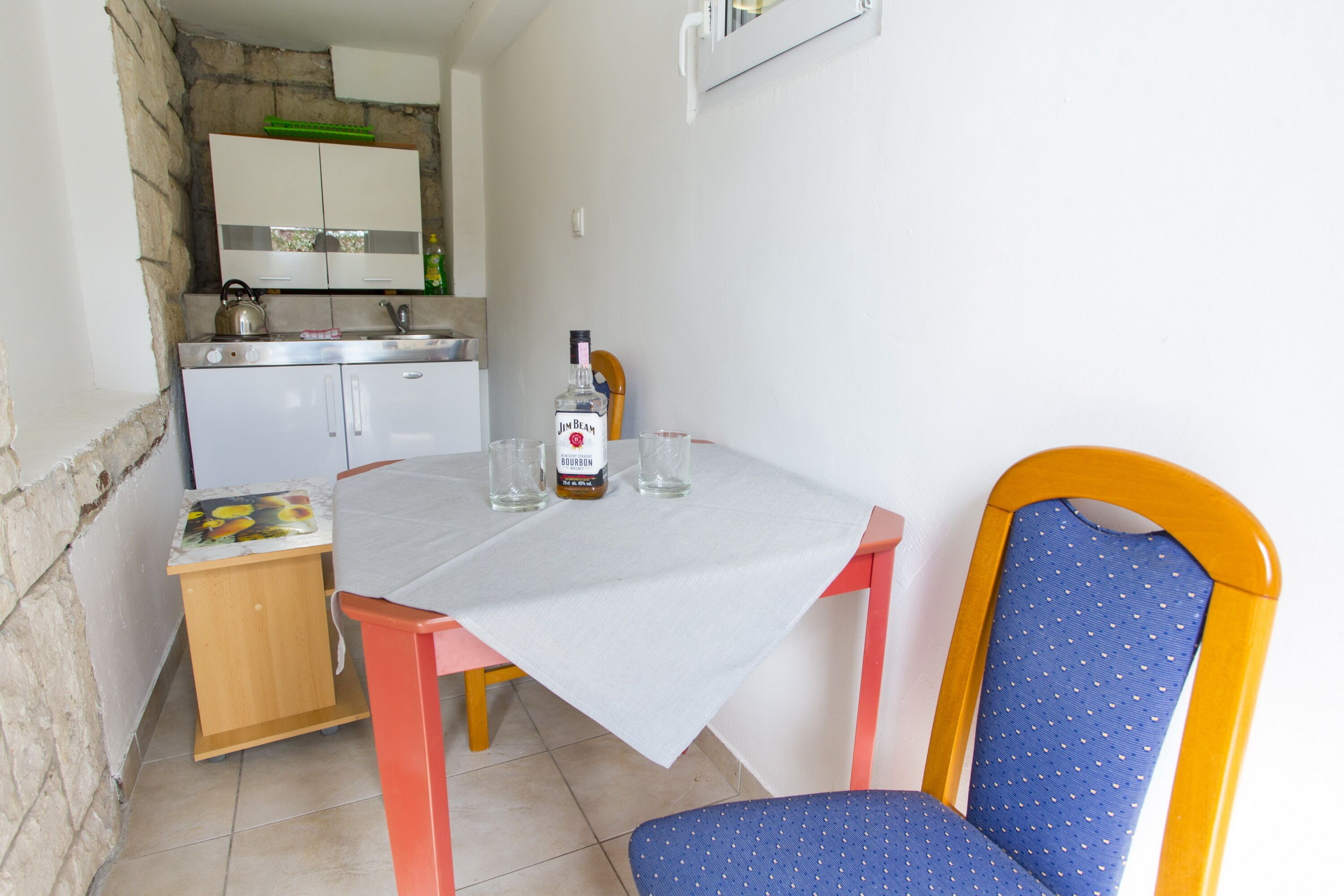 Une petite cuisine avec une table et une chaise, une bouteille de Jim Beam et un petit placard.