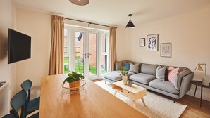 Ein modernes Wohnzimmer mit einer Couch, einem Couchtisch, einem Fernseher und einem Essbereich mit Stühlen und einem Tisch.