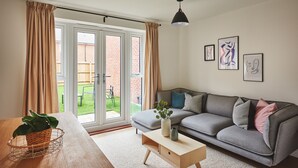 Ein modernes Wohnzimmer mit einem grauen Sofa, einem Holztisch und einer Schiebetür zu einem Garten.