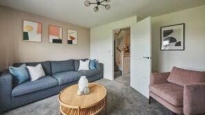 Ein modernes Wohnzimmer mit einem grauen Sofa, einem runden Holztisch und einem rosafarbenen Sessel.