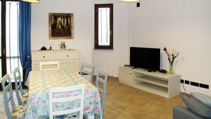 Un coin repas avec une table dressée pour quatre personnes, un téléviseur posé sur un meuble et un tableau accroché au mur.