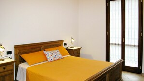 Une chambre à coucher avec un lit en bois, deux tables de chevet avec des lampes, une fenêtre avec des rideaux et un plancher carrelé.