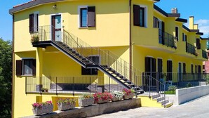 Un bâtiment jaune avec un escalier menant à un balcon, le tout entouré de jardinières fleuries.