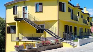 Un edificio amarillo con una escalera que lleva a un balcón, rodeado de macetas con flores.