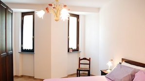 Un dormitorio con cama, una silla, una mesita de noche y una ventana.