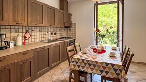 Una cocina con armarios de madera, salpicadero de azulejos y una mesa de comedor con mantel colorido.